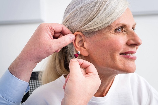 Seniorin lächelt, während ihr ein Hörgerät vom Hörakustiker ins Ohr eingesetzt wird.